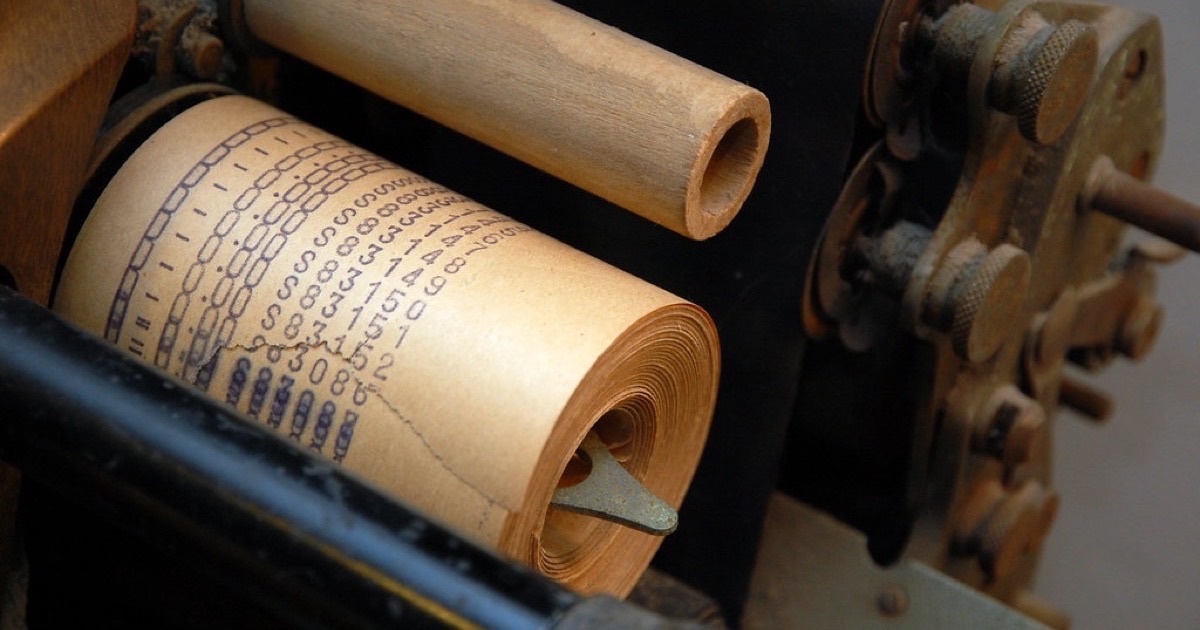 Close-up of a paper till roll printed with rows of figures, wound inside an old cash register
